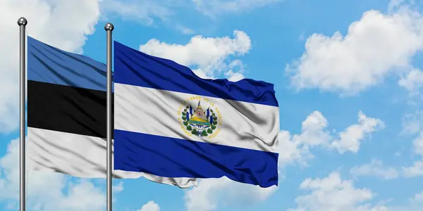 Bandera de Estonia y El Salvador ondeando en el viento contra el cielo azul nublado blanco juntos. Concepto diplomático, relaciones internacionales . — Foto de Stock