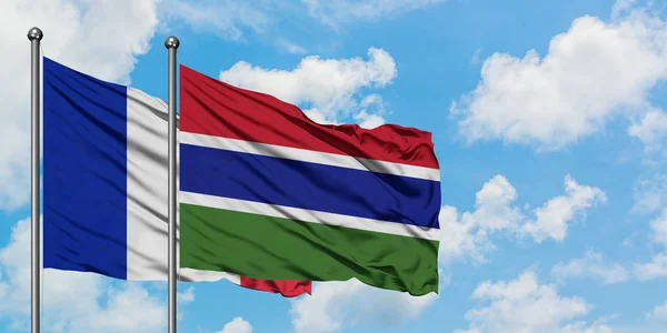 Bandera de Francia y Gambia ondeando en el viento contra el cielo azul nublado blanco juntos. Concepto diplomático, relaciones internacionales . — Foto de Stock