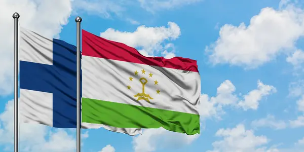 Bandera de Finlandia y Tayikistán ondeando en el viento contra el cielo azul nublado blanco juntos. Concepto diplomático, relaciones internacionales . — Foto de Stock