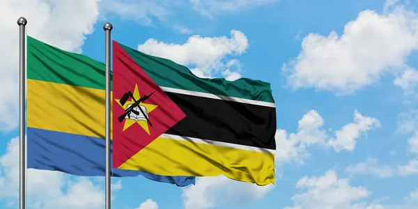 Bandera de Gabón y Mozambique ondeando en el viento contra el cielo azul nublado blanco juntos. Concepto diplomático, relaciones internacionales . — Foto de Stock