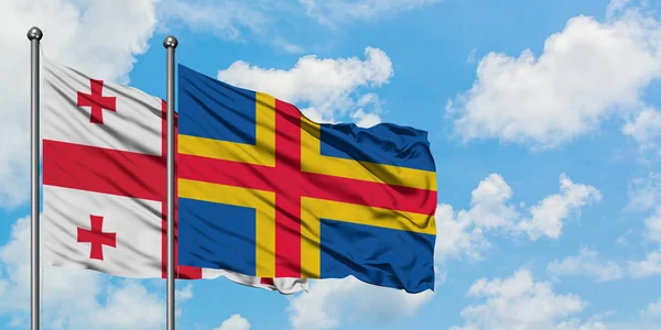 Vlajka Gruzie a Aland Islands se ve větru vlní proti bíle zatažené modré obloze. Diplomacie, mezinárodní vztahy. — Stock fotografie