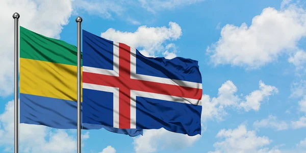 Bandera de Gabón e Islandia ondeando en el viento contra el cielo azul nublado blanco juntos. Concepto diplomático, relaciones internacionales . — Foto de Stock