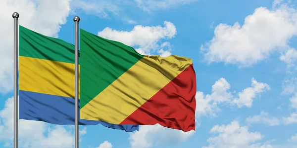 Gabón y la República del Congo ondean en el viento contra el cielo azul nublado blanco juntos. Concepto diplomático, relaciones internacionales . — Foto de Stock