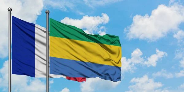 Bandera de Francia y Gabón ondeando en el viento contra el cielo azul nublado blanco juntos. Concepto diplomático, relaciones internacionales . — Foto de Stock