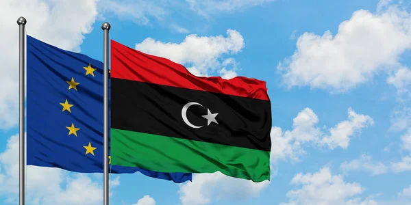 Bandera de la Unión Europea y Libia ondeando en el viento contra el cielo azul nublado blanco juntos. Concepto diplomático, relaciones internacionales . — Foto de Stock