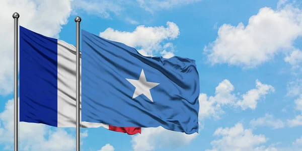 A bandeira da França e da Somália agitando no vento contra o céu azul nublado branco juntos. Conceito de diplomacia, relações internacionais . — Fotografia de Stock
