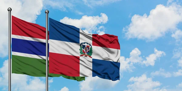 Bandera de Gambia y República Dominicana ondeando en el viento contra el cielo azul nublado blanco juntos. Concepto diplomático, relaciones internacionales . — Foto de Stock