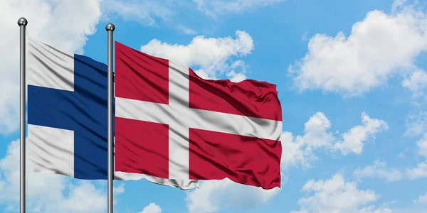 Drapeau de la Finlande et du Danemark agitant dans le vent contre ciel bleu nuageux blanc ensemble. Concept de diplomatie, relations internationales . — Photo