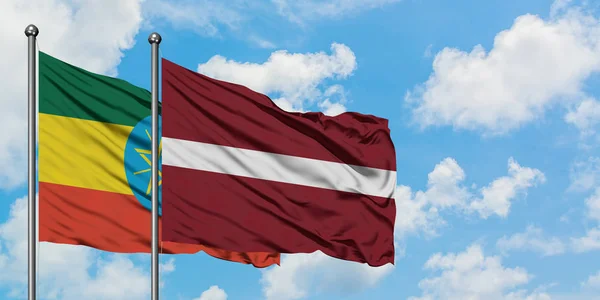 Bandera de Etiopía y Letonia ondeando en el viento contra el cielo azul nublado blanco juntos. Concepto diplomático, relaciones internacionales . — Foto de Stock