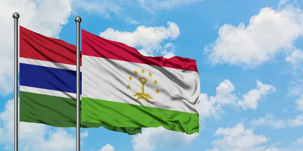 Bandera de Gambia y Tayikistán ondeando en el viento contra el cielo azul nublado blanco juntos. Concepto diplomático, relaciones internacionales . — Foto de Stock