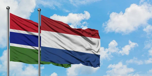 一緒に白い曇り青い空に対して風に手を振るガンビアとオランダの旗。外交概念、国際関係. — ストック写真