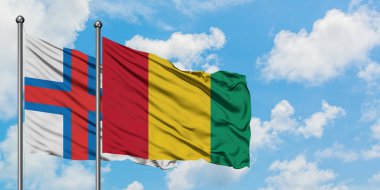 Faroe Adaları ve Gine bayrağı birlikte beyaz bulutlu mavi gökyüzüne karşı rüzgarda sallayarak. Diplomasi kavramı, uluslararası ilişkiler.