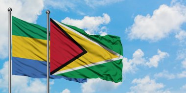 Gabon ve Guyana bayrağı birlikte beyaz bulutlu mavi gökyüzüne karşı rüzgarda sallayarak. Diplomasi kavramı, uluslararası ilişkiler.