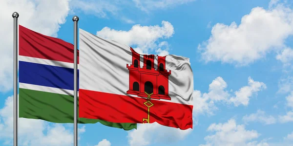 Gâmbia e Gibraltar acenando com o vento contra o céu azul nublado branco juntos. Conceito de diplomacia, relações internacionais . — Fotografia de Stock