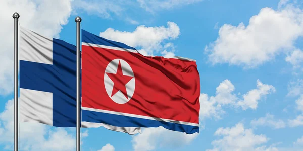 Bandera de Finlandia y Corea del Norte ondeando en el viento contra el cielo azul nublado blanco juntos. Concepto diplomático, relaciones internacionales . — Foto de Stock