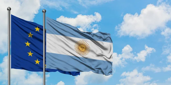 Bandera de la Unión Europea y Argentina ondeando en el viento contra el cielo azul nublado blanco juntos. Concepto diplomático, relaciones internacionales . — Foto de Stock