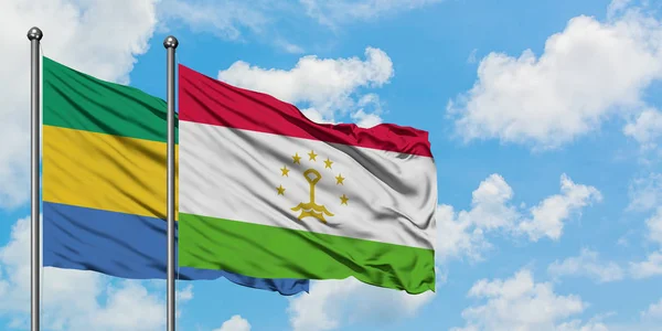 Bandera de Gabón y Tayikistán ondeando en el viento contra el cielo azul nublado blanco juntos. Concepto diplomático, relaciones internacionales . — Foto de Stock