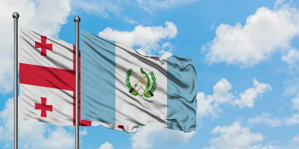 Bandera de Georgia y Guatemala ondeando en el viento contra el cielo azul nublado blanco juntos. Concepto diplomático, relaciones internacionales . — Foto de Stock