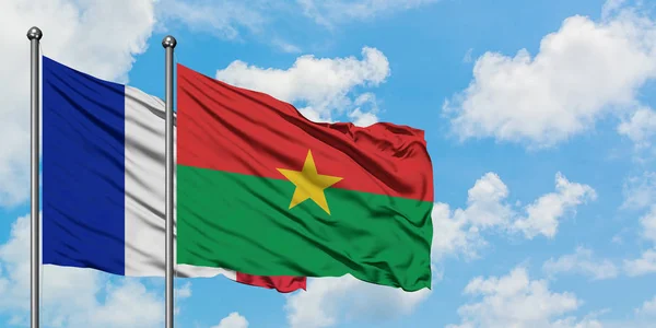 Bandera de Francia y Burkina Faso ondeando en el viento contra el cielo azul nublado blanco juntos. Concepto diplomático, relaciones internacionales . — Foto de Stock