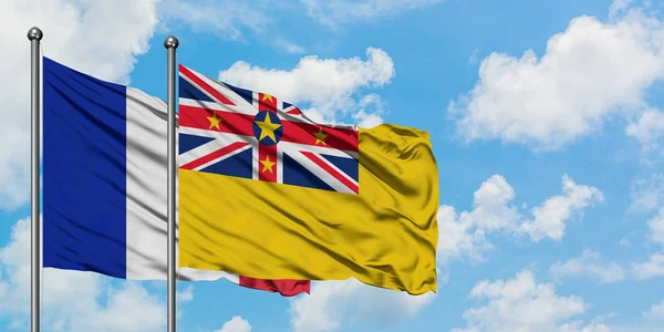 Bandera de Francia y Niue ondeando en el viento contra el cielo azul nublado blanco juntos. Concepto diplomático, relaciones internacionales . — Foto de Stock