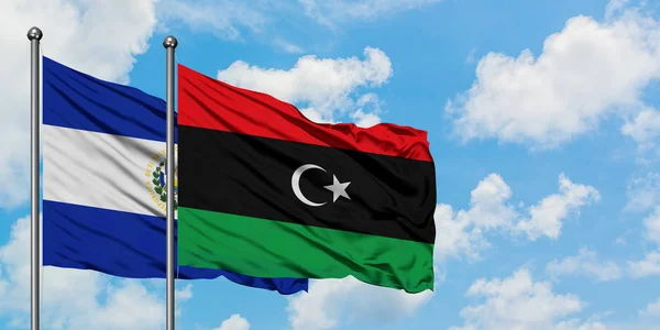 Bandera de El Salvador y Libia ondeando en el viento contra el cielo azul nublado blanco juntos. Concepto diplomático, relaciones internacionales . — Foto de Stock