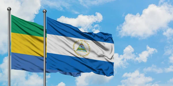 Bandera de Gabón y Nicaragua ondeando en el viento contra el cielo azul nublado blanco juntos. Concepto diplomático, relaciones internacionales . —  Fotos de Stock