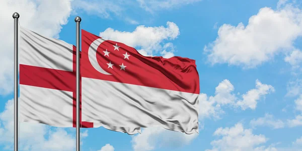 Bandera de Inglaterra y Singapur ondeando en el viento contra el cielo azul nublado blanco juntos. Concepto diplomático, relaciones internacionales . —  Fotos de Stock