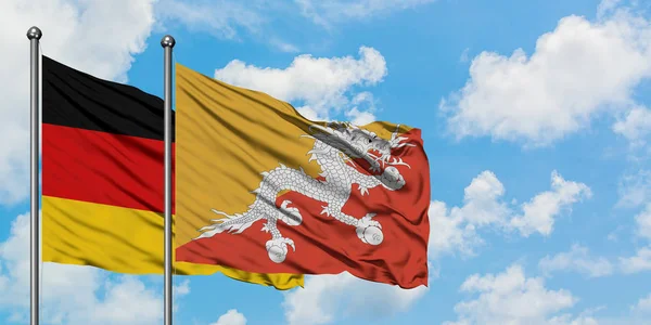 Germania e bandiera del Bhutan sventolano nel vento contro il bianco cielo blu nuvoloso insieme. Concetto di diplomazia, relazioni internazionali . — Foto Stock