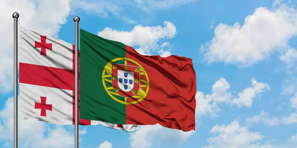 Georgien och Portugal sjunker vifta i vinden mot vit grumlig blå himmel tillsammans. Diplomatisk koncept, internationella relationer. — Stockfoto