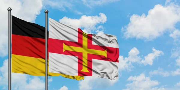 Germania e bandiera Guernsey sventolano insieme nel vento contro il bianco cielo blu nuvoloso. Concetto di diplomazia, relazioni internazionali . — Foto Stock