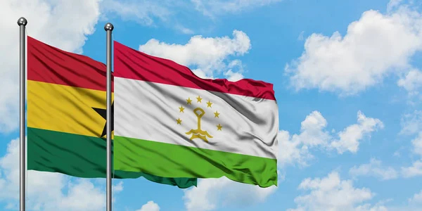 Bandera de Ghana y Tayikistán ondeando en el viento contra el cielo azul nublado blanco juntos. Concepto diplomático, relaciones internacionales . — Foto de Stock