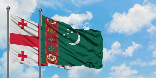 Bandera de Georgia y Turkmenistán ondeando en el viento contra el cielo azul nublado blanco juntos. Concepto diplomático, relaciones internacionales . — Foto de Stock