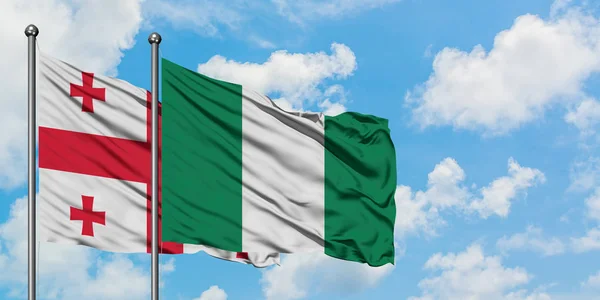 Bandera de Georgia y Nigeria ondeando en el viento contra el cielo azul nublado blanco juntos. Concepto diplomático, relaciones internacionales . — Foto de Stock