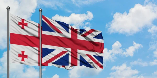Georgien och Storbritannien flagga vifta i vinden mot vit grumlig blå himmel tillsammans. Diplomatisk koncept, internationella relationer. — Stockfoto