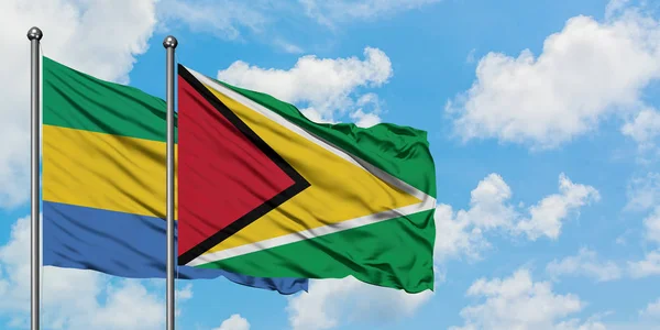 Gabón y Guyana bandera ondeando en el viento contra el cielo azul nublado blanco juntos. Concepto diplomático, relaciones internacionales . — Foto de Stock