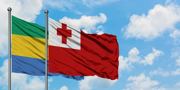 Bandera de Gabón y Tonga ondeando en el viento contra el cielo azul nublado blanco juntos. Concepto diplomático, relaciones internacionales . — Foto de Stock