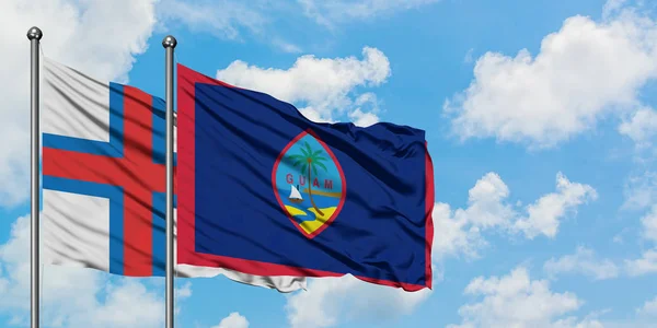 Les îles Féroé et le drapeau Guam agitant dans le vent contre le ciel bleu nuageux blanc ensemble. Concept de diplomatie, relations internationales . — Photo