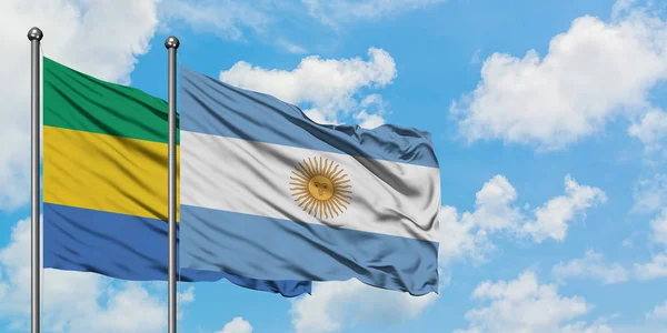 Bandera de Gabón y Argentina ondeando en el viento contra el cielo azul nublado blanco juntos. Concepto diplomático, relaciones internacionales . — Foto de Stock