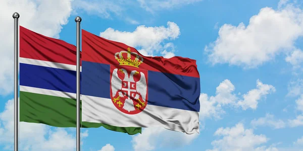 Bandera de Gambia y Serbia ondeando en el viento contra el cielo azul nublado blanco juntos. Concepto diplomático, relaciones internacionales . — Foto de Stock