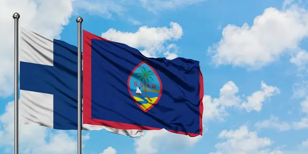 Bandera de Finlandia y Guam ondeando en el viento contra el cielo azul nublado blanco juntos. Concepto diplomático, relaciones internacionales . — Foto de Stock
