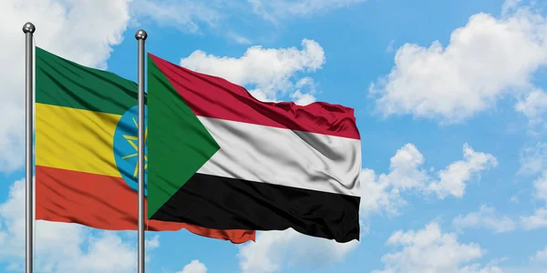 Bandera de Etiopía y Sudán ondeando en el viento contra el cielo azul nublado blanco juntos. Concepto diplomático, relaciones internacionales . — Foto de Stock