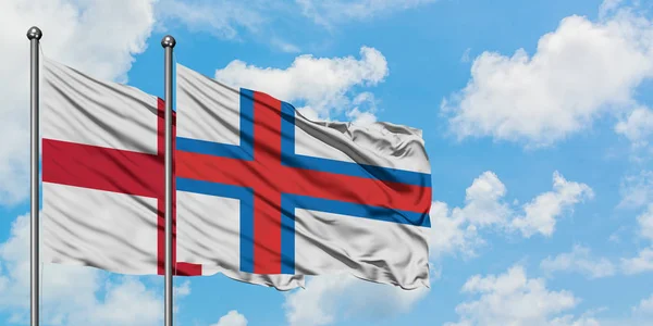 Bandera de Inglaterra y las Islas Feroe ondeando en el viento contra el cielo azul nublado blanco juntos. Concepto diplomático, relaciones internacionales . — Foto de Stock