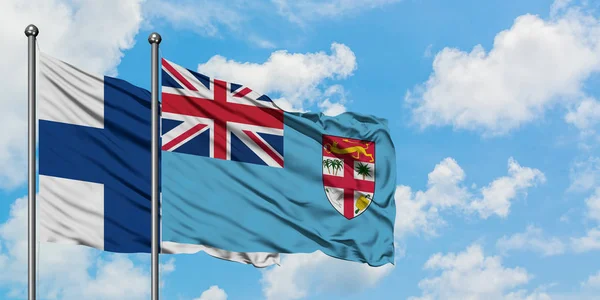 Finlândia e Fiji acenando com o vento contra o céu azul nublado branco juntos. Conceito de diplomacia, relações internacionais . — Fotografia de Stock