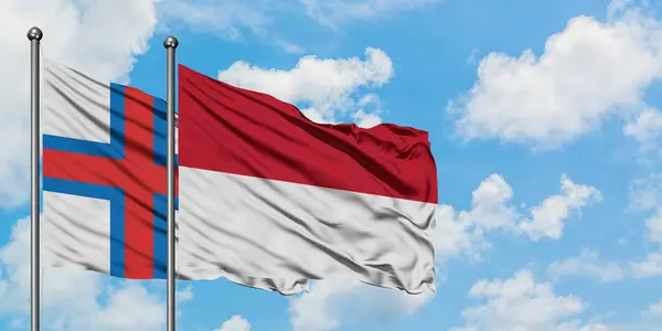Faerské ostrovy a Indonésie vlají ve větru proti bíle zatažené modré obloze. Diplomacie, mezinárodní vztahy. — Stock fotografie