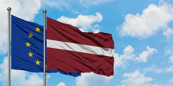Bandera de la Unión Europea y Letonia ondeando en el viento contra el cielo azul nublado blanco juntos. Concepto diplomático, relaciones internacionales . — Foto de Stock