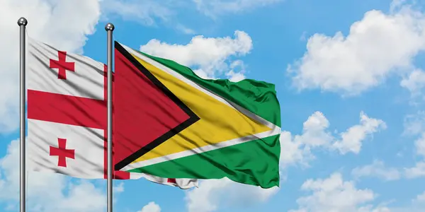 Bandera de Georgia y Guyana ondeando en el viento contra el cielo azul nublado blanco juntos. Concepto diplomático, relaciones internacionales . — Foto de Stock