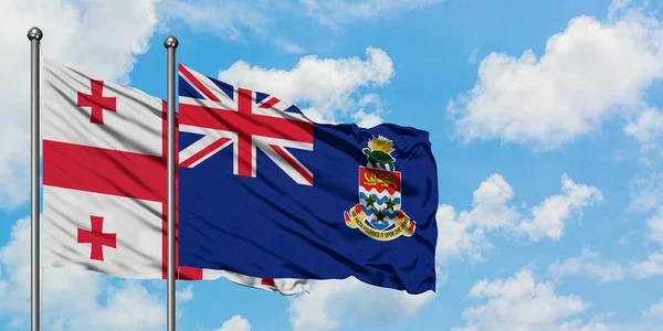 Georgia e Isole Cayman bandiera sventolando nel vento contro bianco cielo blu nuvoloso insieme. Concetto di diplomazia, relazioni internazionali . — Foto Stock