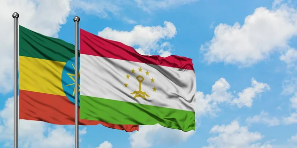 Etiopía y Tayikistán ondean en el viento contra el cielo azul nublado blanco juntos. Concepto diplomático, relaciones internacionales . — Foto de Stock
