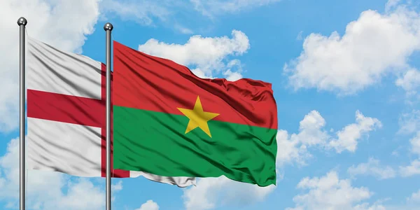 Bandera de Inglaterra y Burkina Faso ondeando en el viento contra el cielo azul nublado blanco juntos. Concepto diplomático, relaciones internacionales . — Foto de Stock