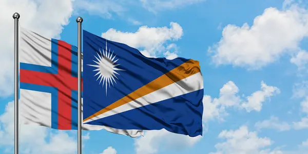 Feröer-szigetek és a Marshall-szigetek zászló integetett a szél ellen, fehér felhős kék ég együtt. Diplomáciai koncepció, nemzetközi kapcsolatok. — Stock Fotó